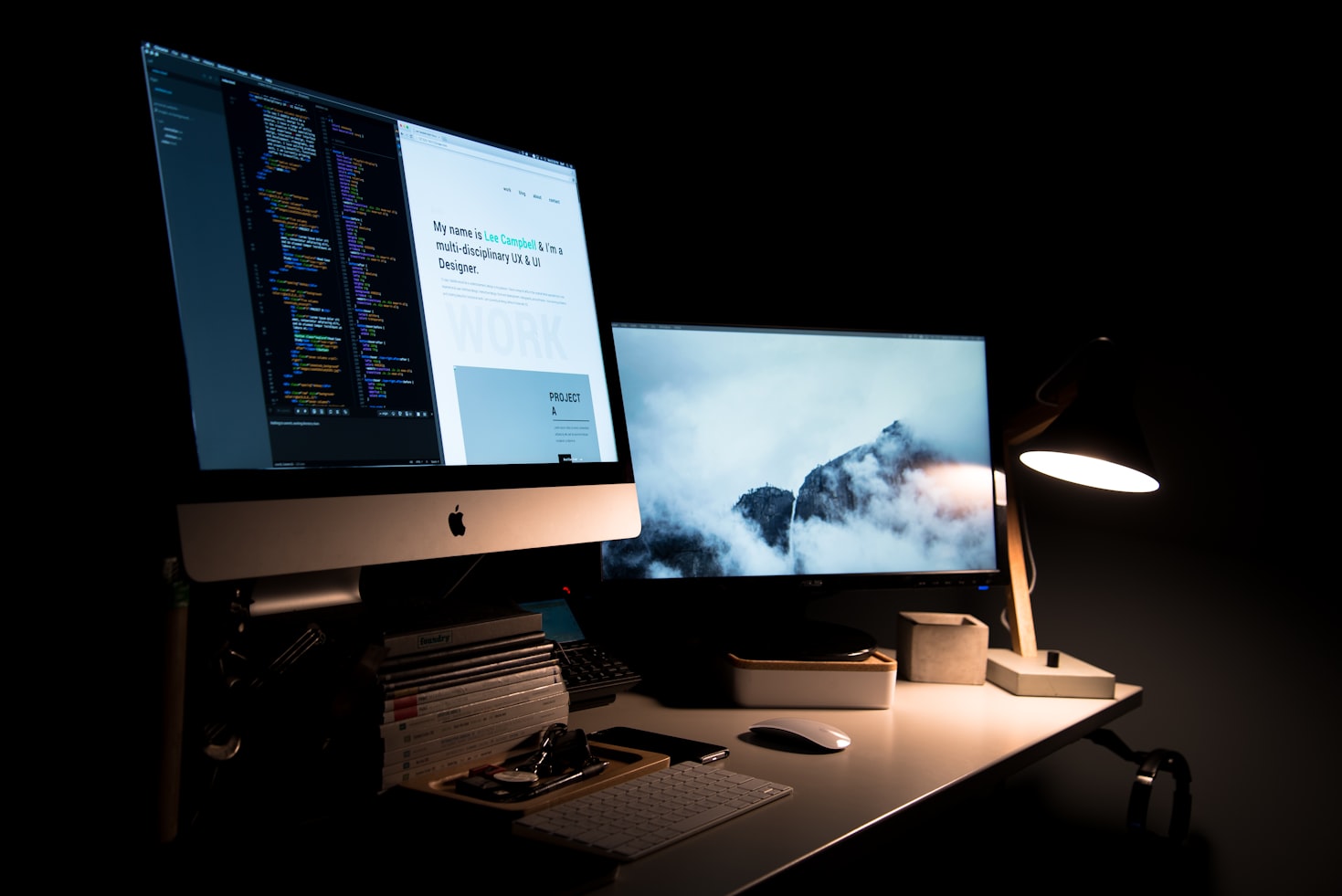 A productive desk in a dark room with Mac desktops displaying code