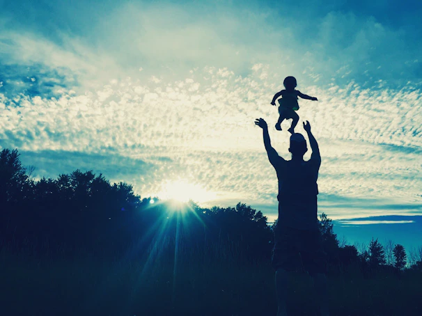 A silhouette of a father lifting his daughter high against a soft, warm sky.