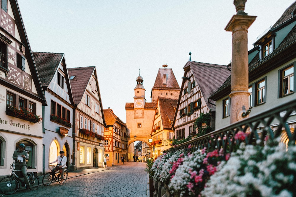 flores de pétalos blancos y rosados en la cerca de metal cerca de las casas de hormigón y la torre durante el día