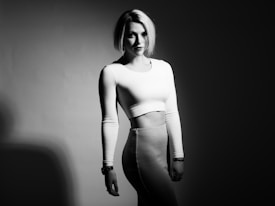 A woman stands confidently in a black and white photograph. She is wearing a fitted long-sleeved crop top and a matching high-waisted skirt. Her hair is styled in a sleek bob, and she gazes directly at the camera.