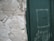 A weathered wall with peeling plaster stands next to a green door with the word 'HOSTEL' written on it. The door shows signs of wear, with scuff marks and faded paint, adding to the overall aged appearance of the scene.