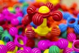 Colorful interlocking plastic toys are scattered in a pile, predominantly featuring bright colors such as pink, red, yellow, blue, and green. The foreground showcases a structure with ball-and-stick elements, giving a playful and vibrant impression.