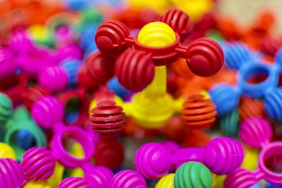 Colorful interlocking plastic toys are scattered in a pile, predominantly featuring bright colors such as pink, red, yellow, blue, and green. The foreground showcases a structure with ball-and-stick elements, giving a playful and vibrant impression.