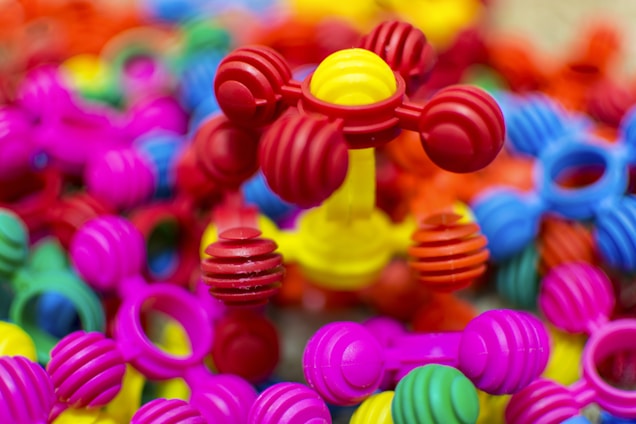 Colorful interlocking plastic toys are scattered in a pile, predominantly featuring bright colors such as pink, red, yellow, blue, and green. The foreground showcases a structure with ball-and-stick elements, giving a playful and vibrant impression.