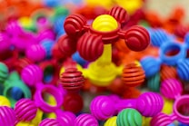 Colorful interlocking plastic toys are scattered in a pile, predominantly featuring bright colors such as pink, red, yellow, blue, and green. The foreground showcases a structure with ball-and-stick elements, giving a playful and vibrant impression.