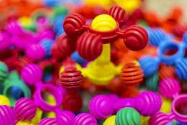 Colorful interlocking plastic toys are scattered in a pile, predominantly featuring bright colors such as pink, red, yellow, blue, and green. The foreground showcases a structure with ball-and-stick elements, giving a playful and vibrant impression.