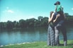 father, mother, and son standing on grass lawn near a body of water during daytime
