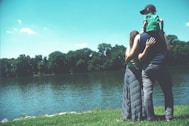 father, mother, and son standing on grass lawn near a body of water during daytime