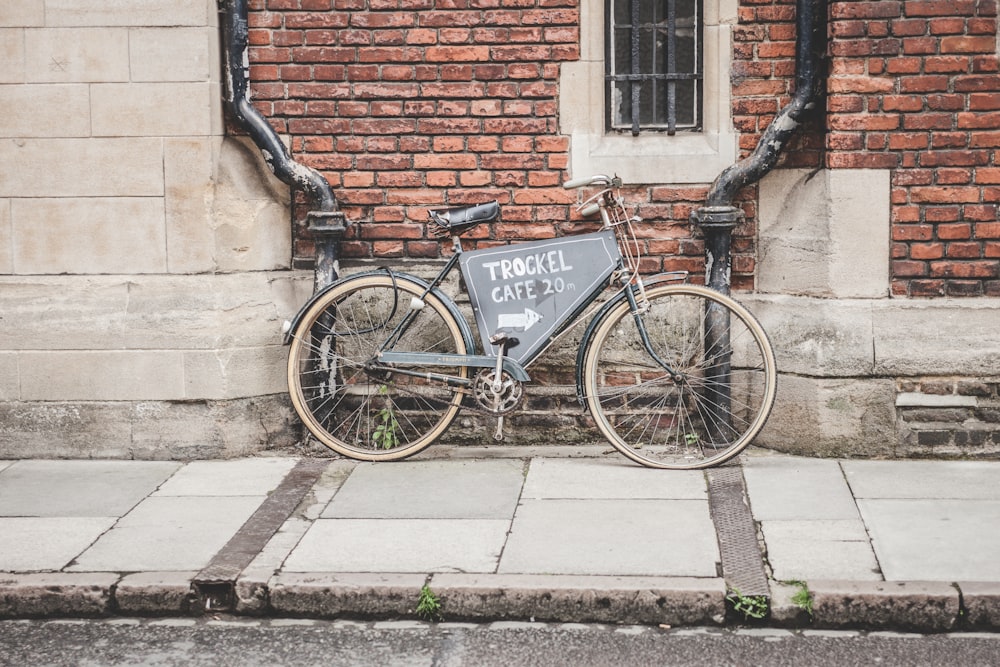 vélo noir s’appuyant sur un mur de béton brun et gris pendant la journée