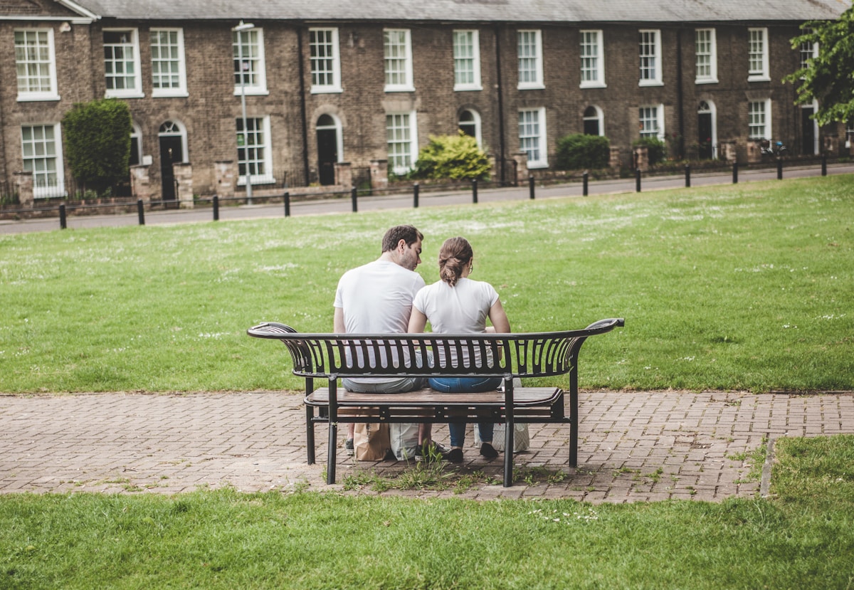 A university student and a younger student sit on a bench discussing a mentoring program.