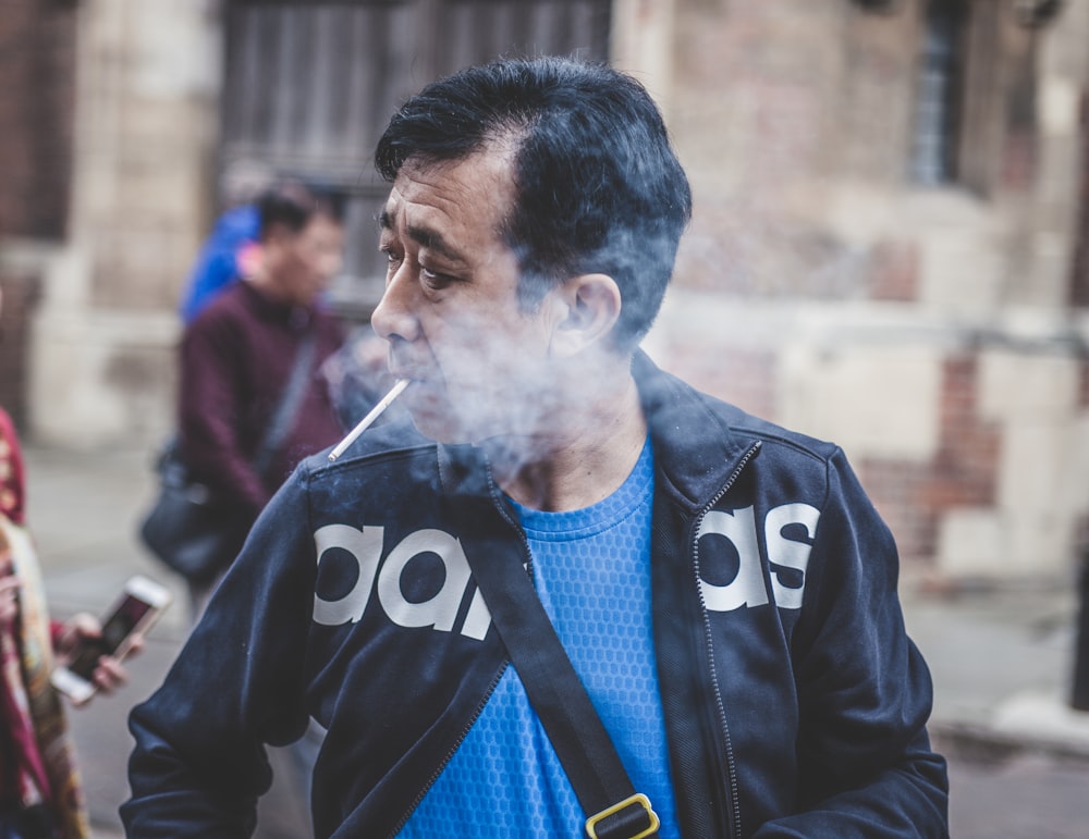 hombre en chaqueta de cuero Adidas negra fumando cigarrillo