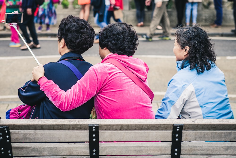 Tres personas tomando selfie mientras están sentadas en un banco durante el día