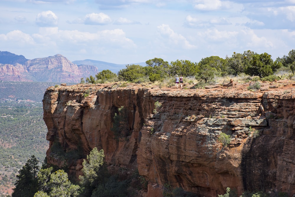 two person walks on brown cliff under clear blue sky during daytime