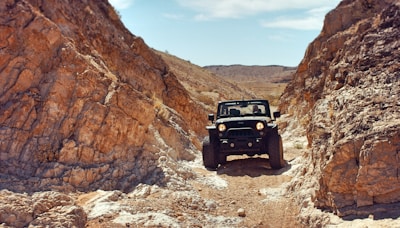 A rugged Mitsubishi Triton climbing a rocky trail under a bright blue sky