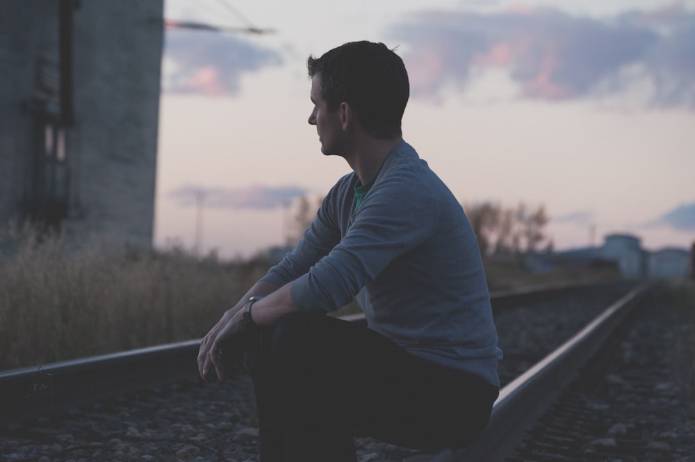 Mann sitzt auf Eisenbahn unter grauem Himmel