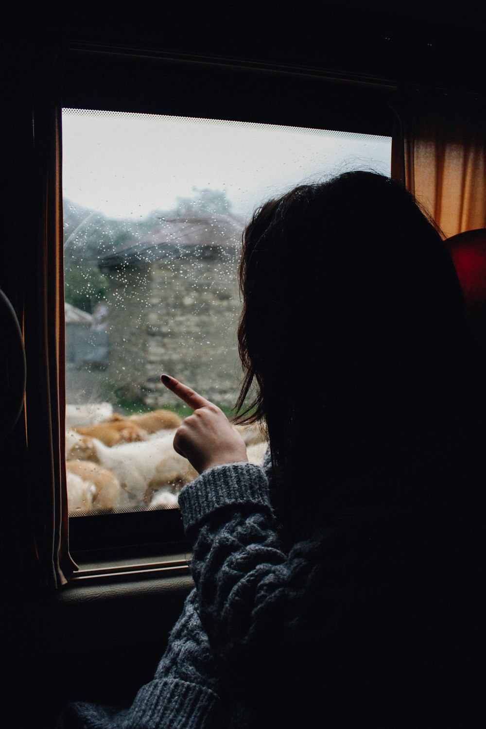 Frau im grauen Strickpullover schaut und zeigt auf das Fenster