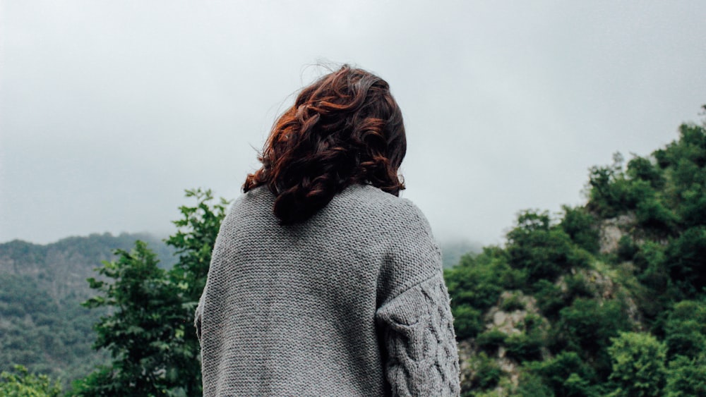 woman in gray sweater standing in front of trees during daytime