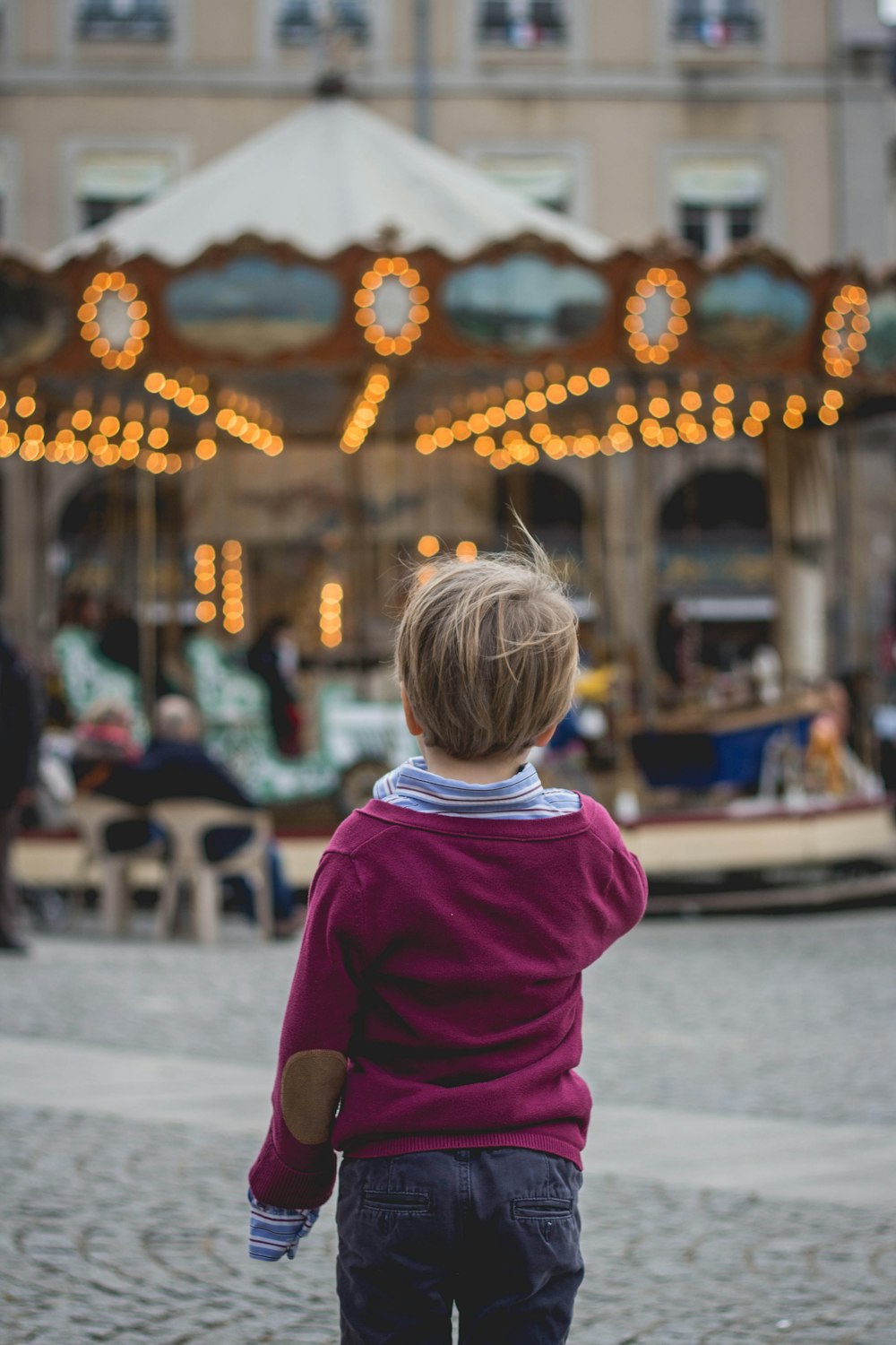 selective focus photography of boy standing in front of carousel