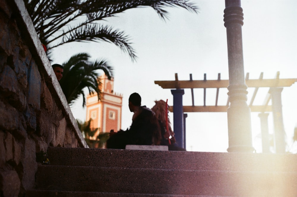 photography of silhouette of man sitting on park bench near concrete stairs