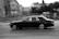 Luxury black car parked on a city street with blurred lights in the background.
