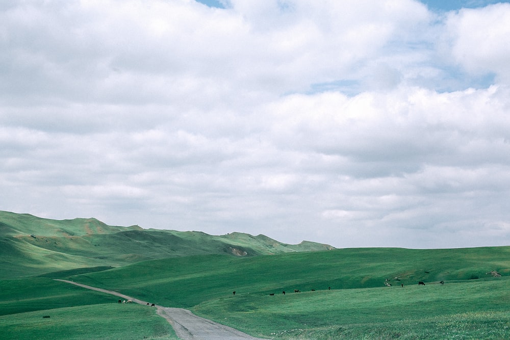 photo of green hill under cloudy white sky