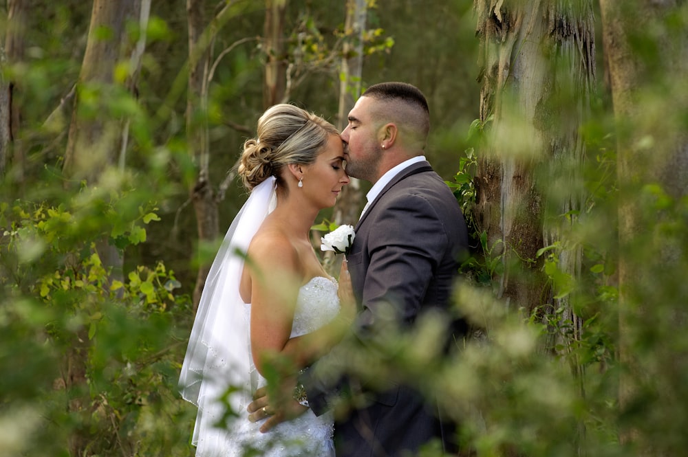 A man kisses a woman's forehead in a forest of trees on their wedding day