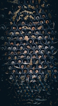 An intricate array of metal objects, possibly decorative ornaments or antique hardware, arranged within cylindrical containers, creating a visually complex pattern. The items exhibit a range of intricate designs, including floral and geometric motifs, set against a dark background that enhances their metallic luster.