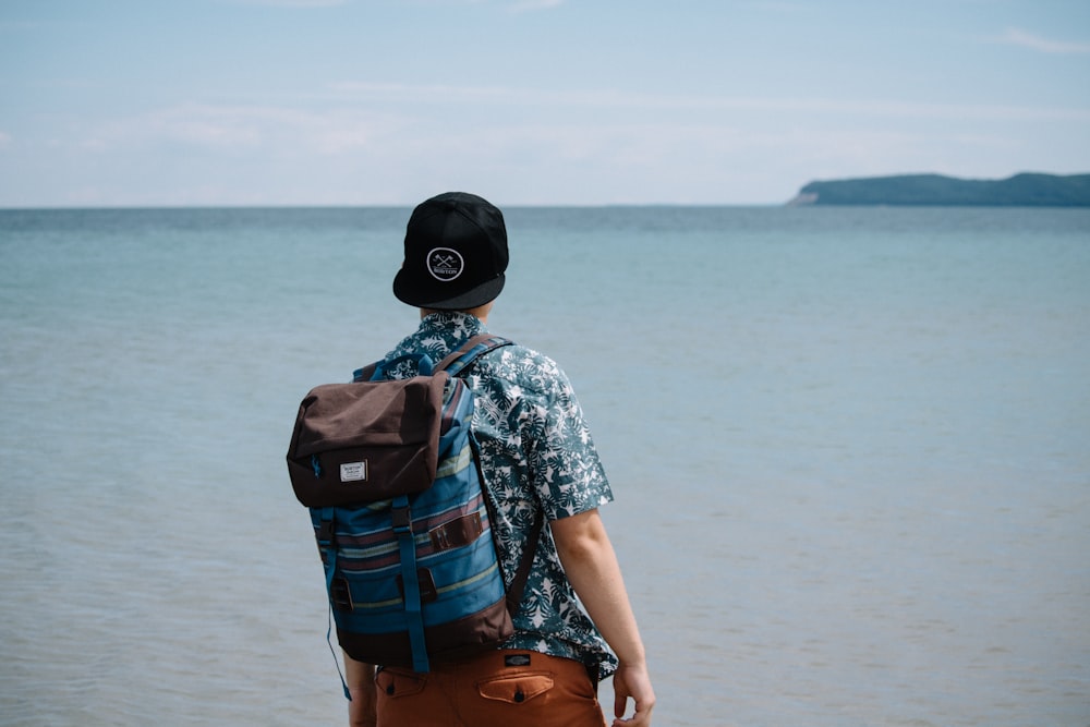 Hombre con mochila azul y negra de pie frente al cuerpo de agua