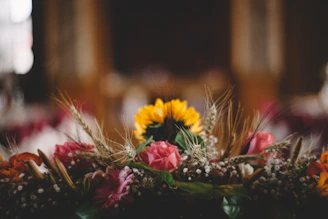 A close-up of a vibrant floral arrangement blending wildflowers and sculptural leaves, bathed in soft natural light.