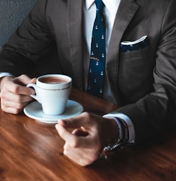 man holding cup filled with coffee on table