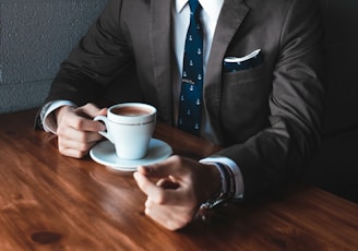 man holding cup filled with coffee on table