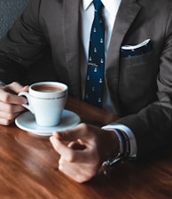 man holding cup filled with coffee on table