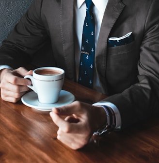 man holding cup filled with coffee on table