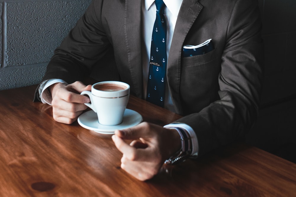 man holding cup filled with coffee on table