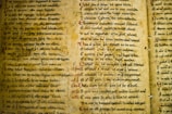 An ancient manuscript with densely handwritten text on aged, yellowed parchment. The text is in a classical font style, with sections highlighted in red ink. The parchment has holes and markings indicative of its age.