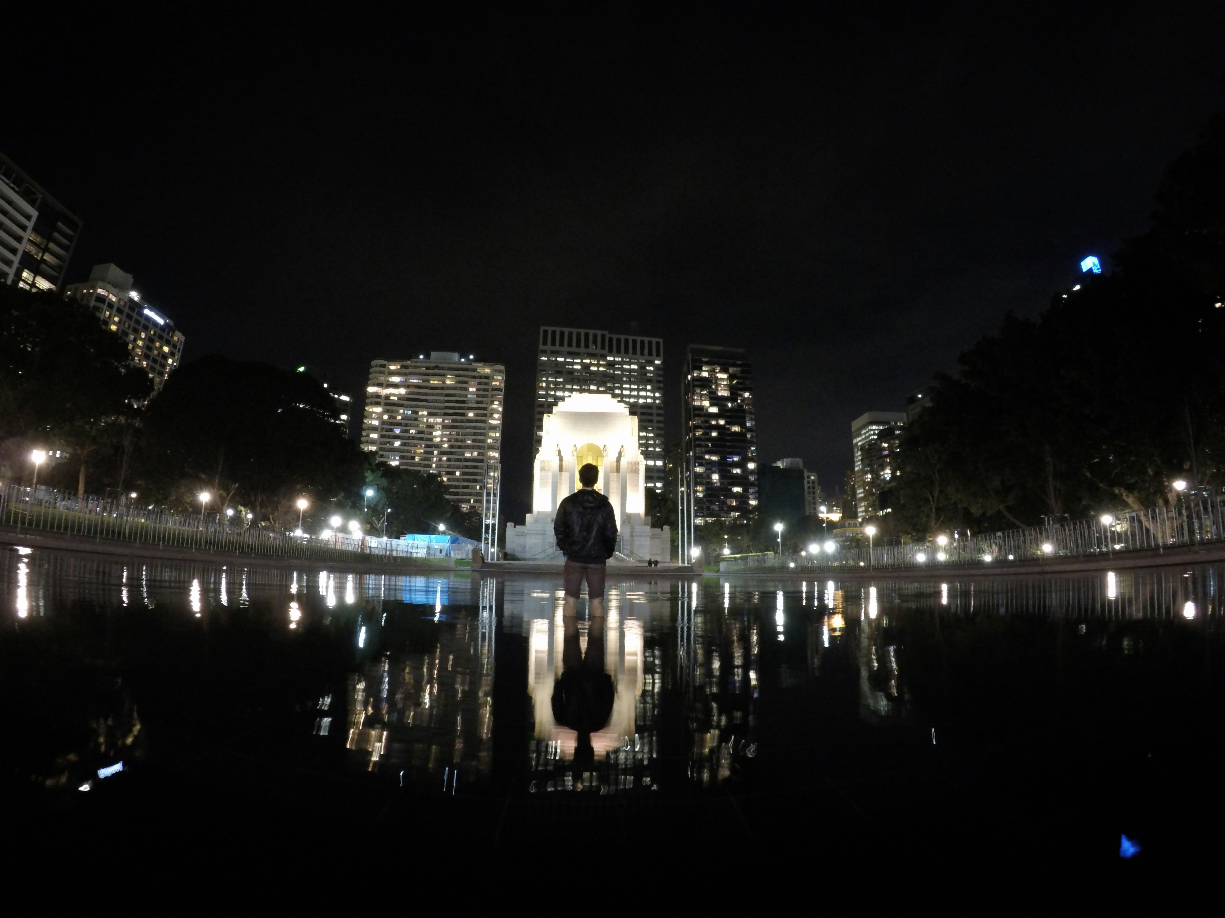 A man wearing a backpack and standing inside a city fountain.