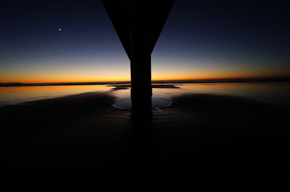 O horizonte beijado pelo sol surge atrás do pilar e do outro lado da água ao entardecer em New Brighton