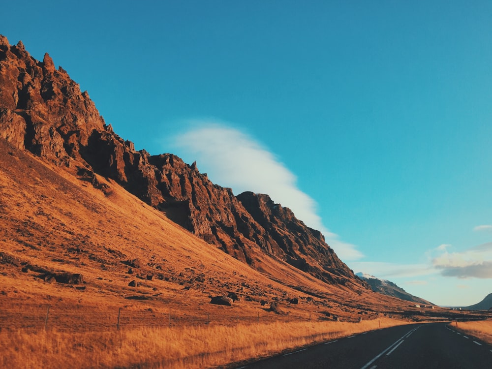 concrete road beside mountain under blue sky