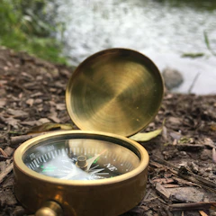 A fragmented compass resting on weathered wood, half-submerged in shadowy water.