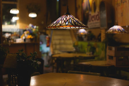 A 3D printed pendant lamp hanging above a rustic wooden table in an African-style cafe with thatch roof.