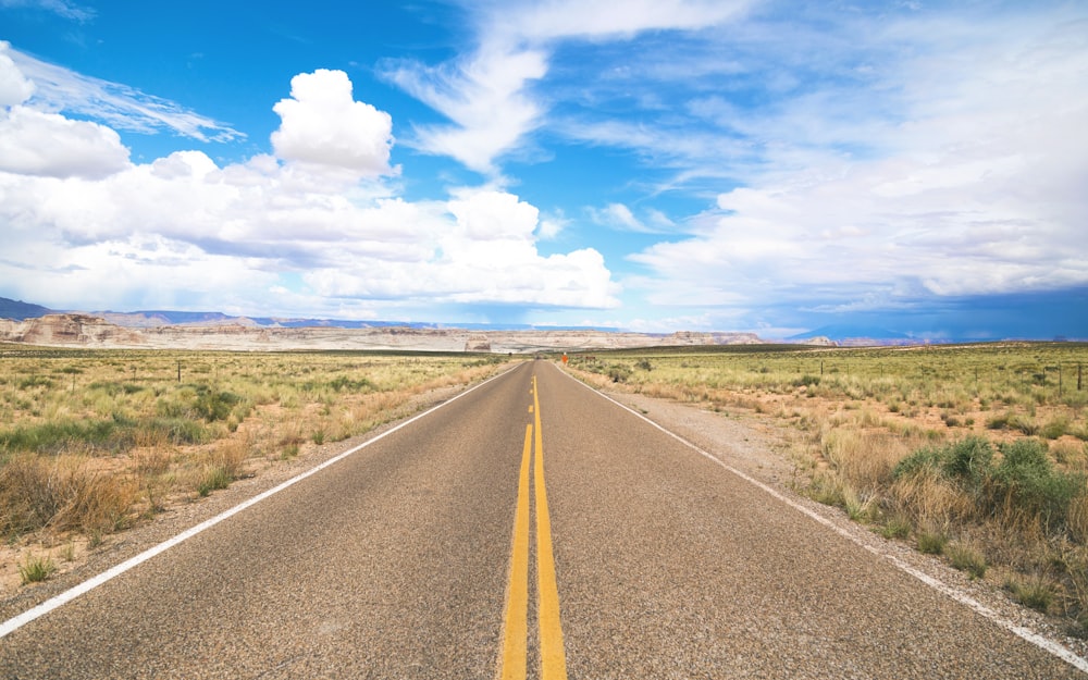 A rural highway surrounded by a desert and meadow with a blue sky filled with fluffy clouds