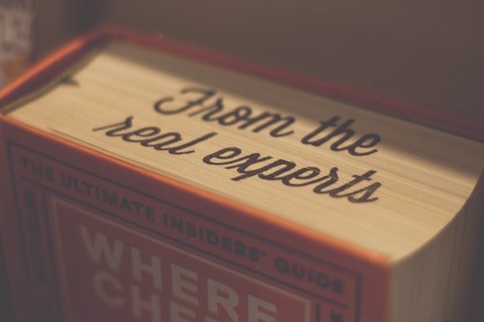 A close-up of a book with the words 'From the real experts' written on the spine. The book has a warm color palette with hints of red and beige, and is titled 'The Ultimate Insiders' Guide' with parts of the title obscured.