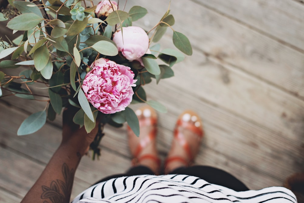 person holding pink flowers standing on brown wooden flooring