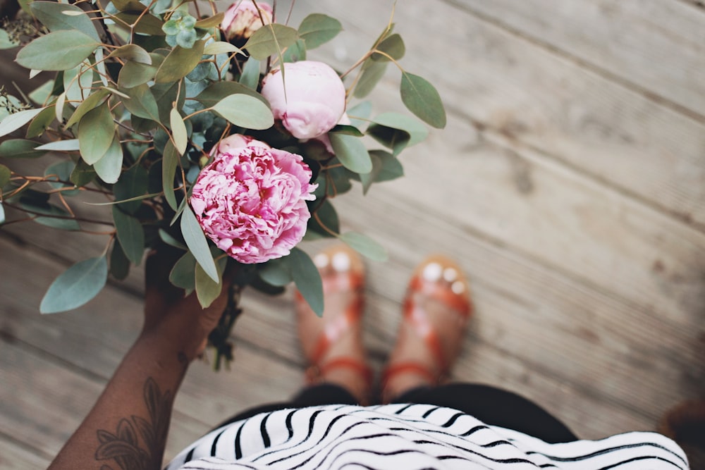Person mit rosa Blumen, die auf braunem Holzboden steht
