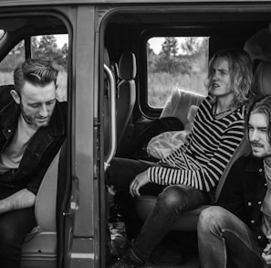 grayscale photo of three men sitting on vehicle seats