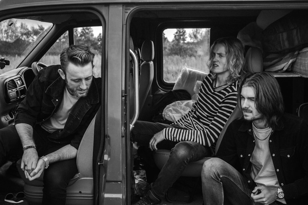 grayscale photo of three men sitting on vehicle seats