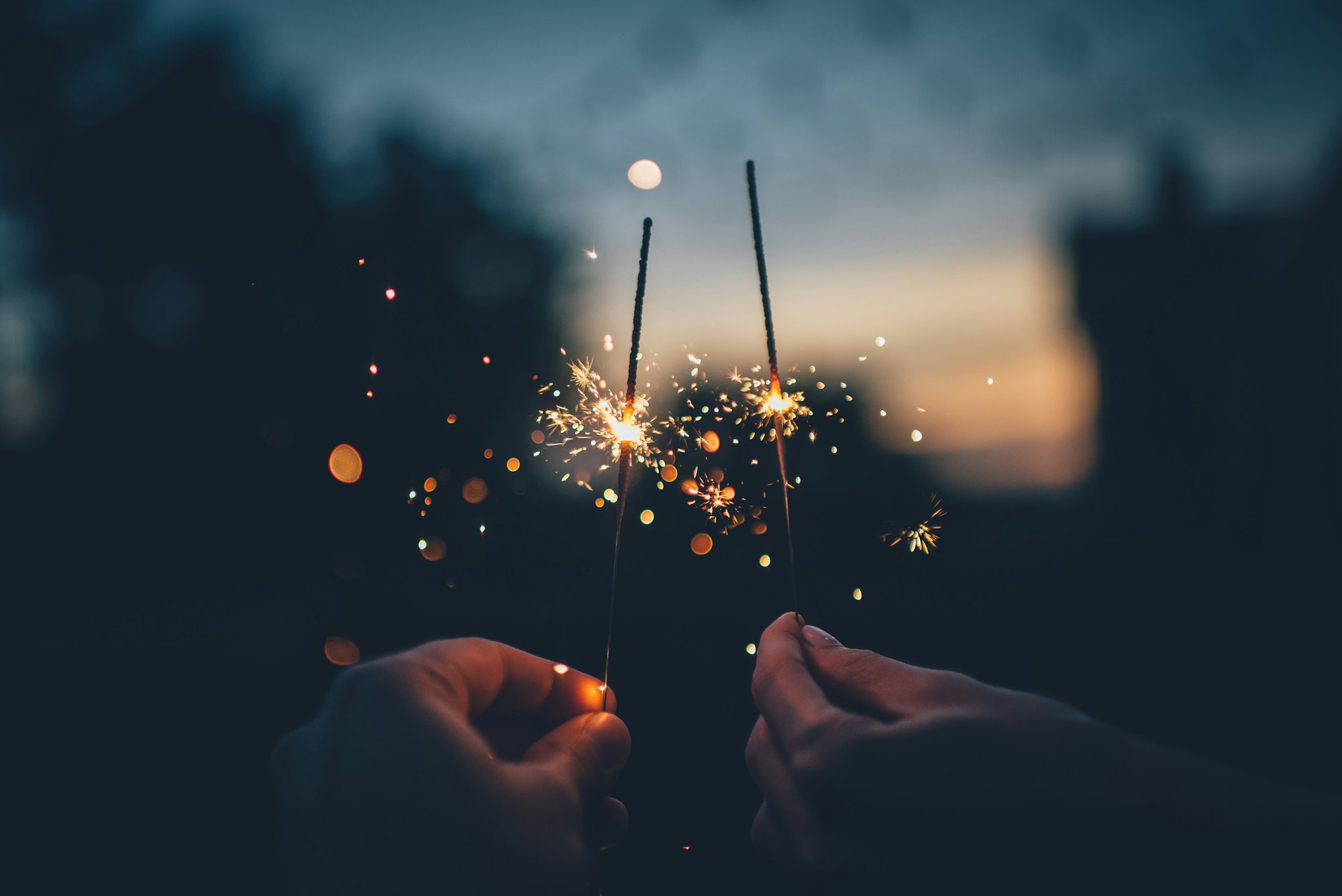 Two hands holding sparklers in the dark