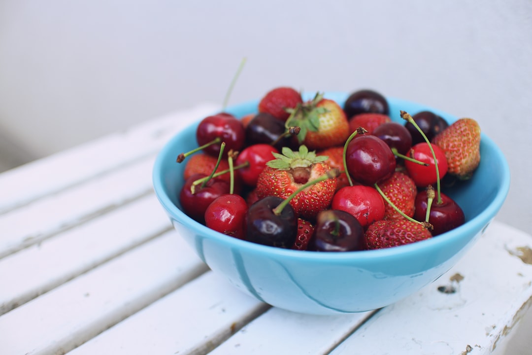 focus photography of strawberries and cherries on blue bowl