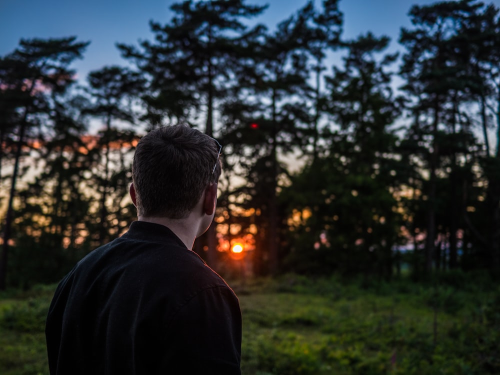 緑の葉の木々の前で夕日を見ている男の写真
