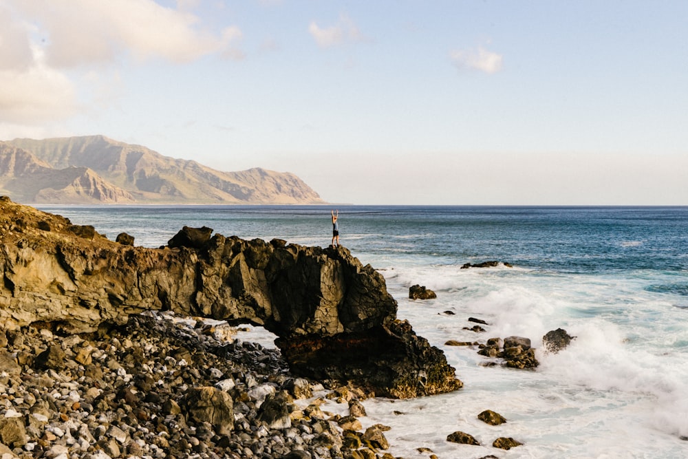 A person standing on the edge of a cliff by the sea with their arms outstretched